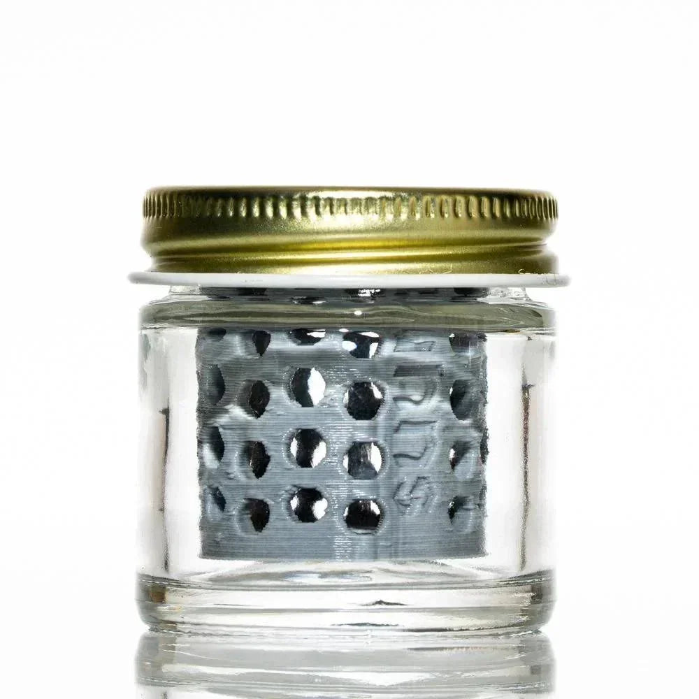 Glass jar with gold lid and internal metal mesh, used as a smoking accessory cleaner.