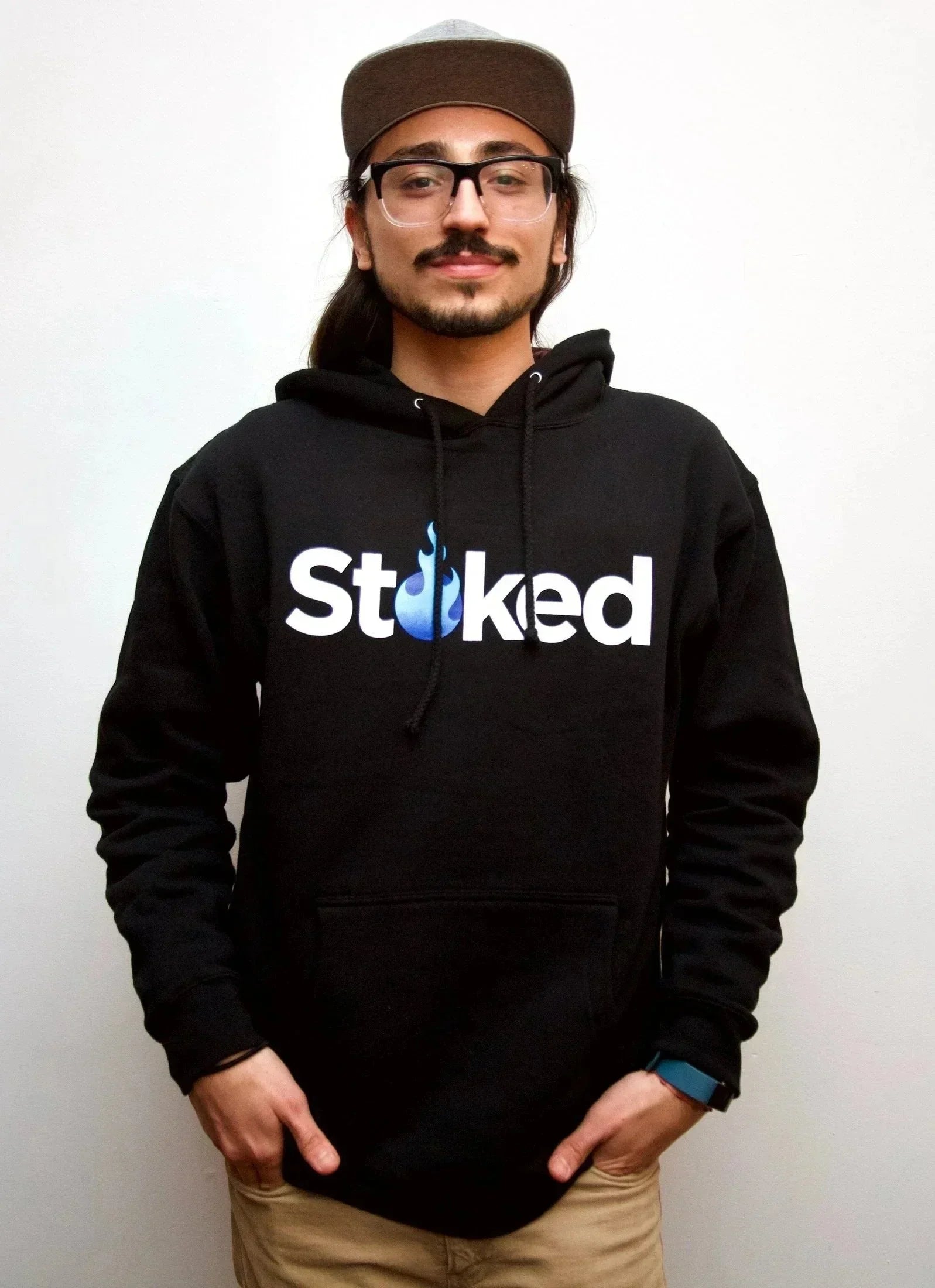 Man in black Stoked hoodie with blue flame logo, wearing glasses and a cap