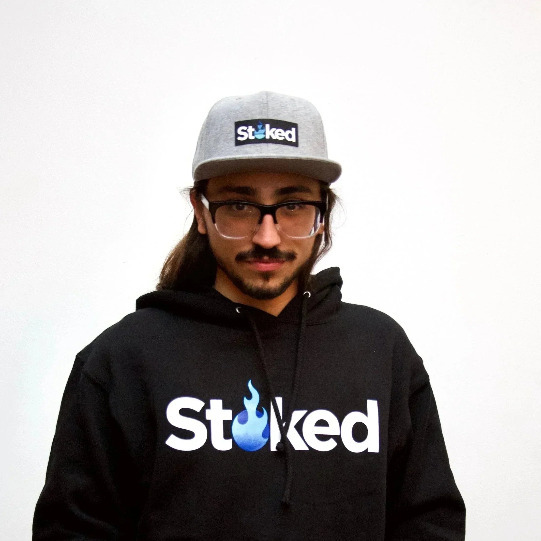 Man in glasses wearing black hoodie and grey hat with 'Stoked' logo on white background