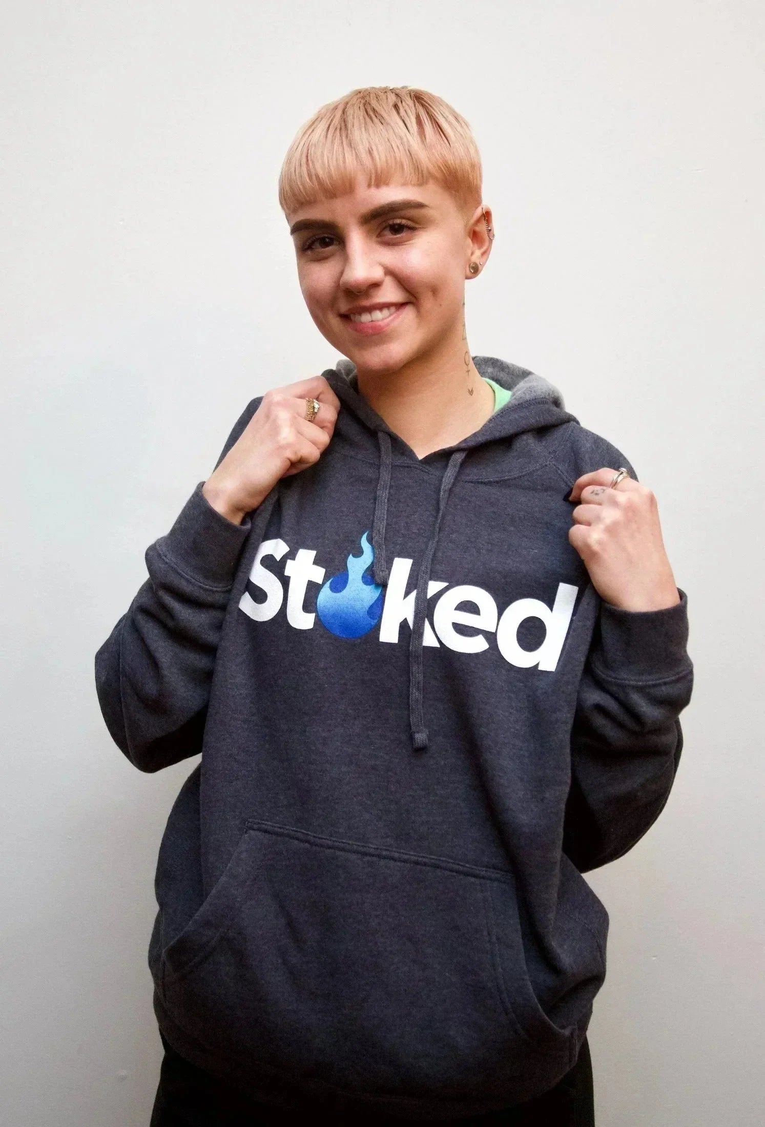 Smiling person wearing a dark hoodie with bold 'Stoked' text and blue flame graphic on front.