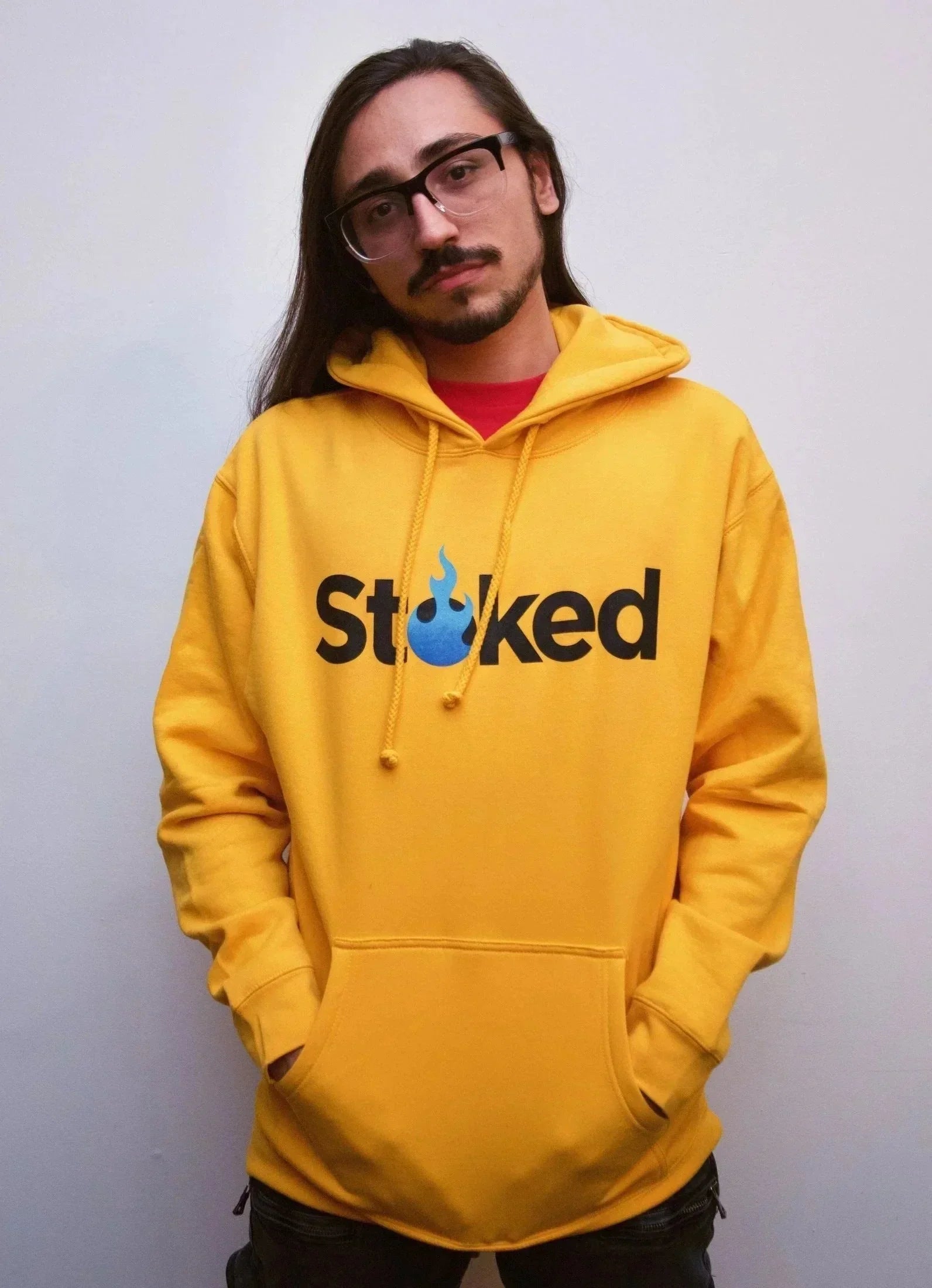 Man wearing a yellow hoodie with Stoked flame logo, hands in pocket, casual streetwear