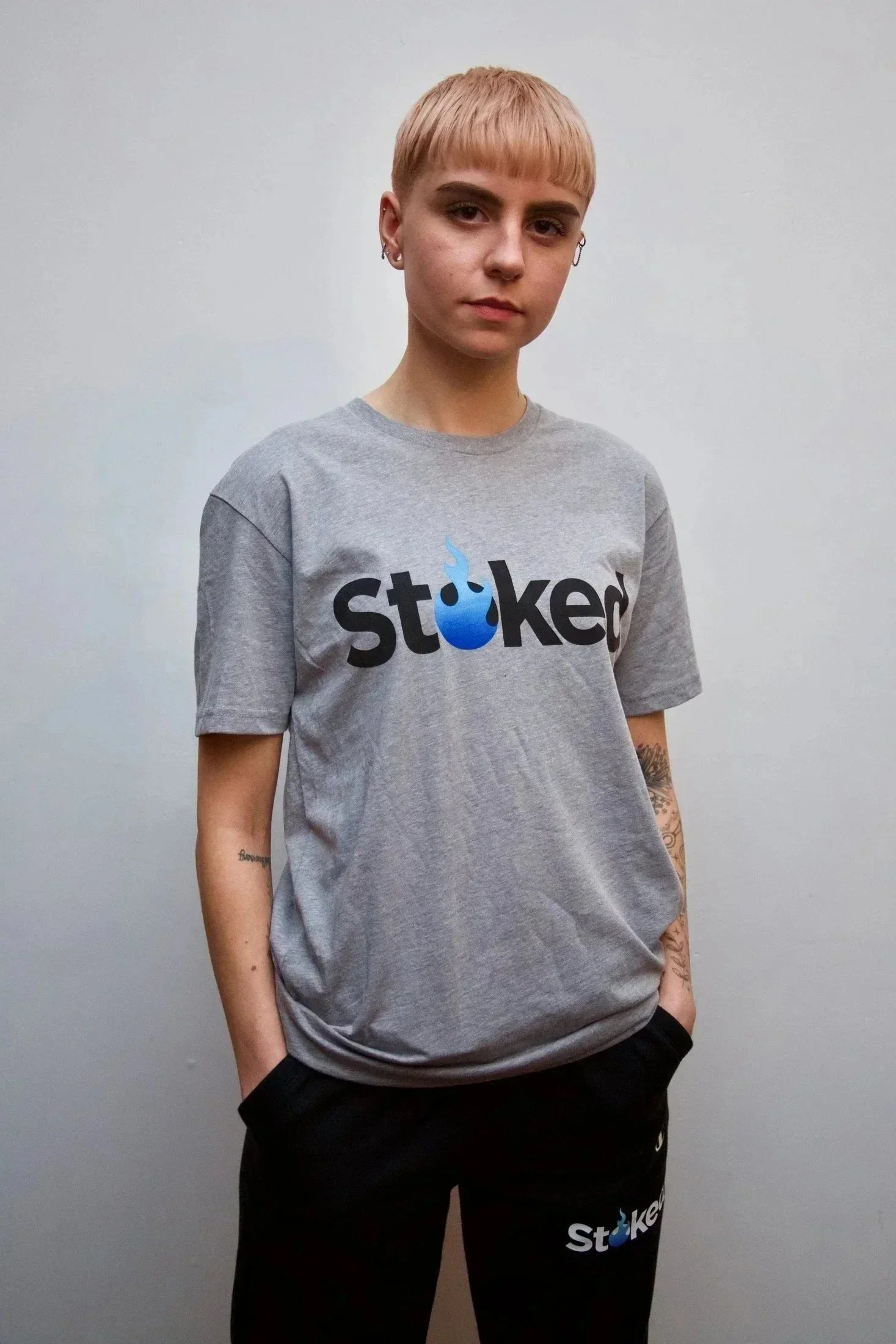 Person wearing gray Stoked logo t-shirt and black pants, standing against plain background