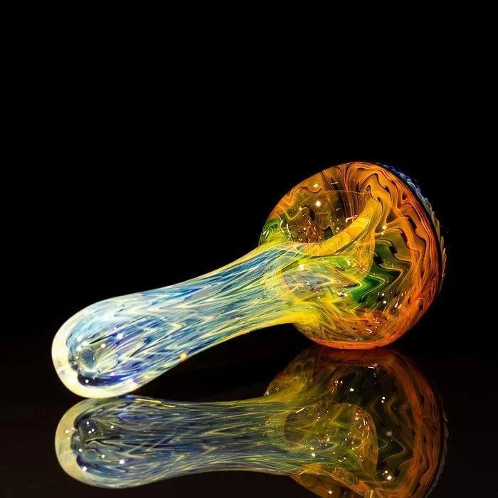 Colorful heady glass spoon pipe with swirls of blue, yellow, and orange on black reflective surface