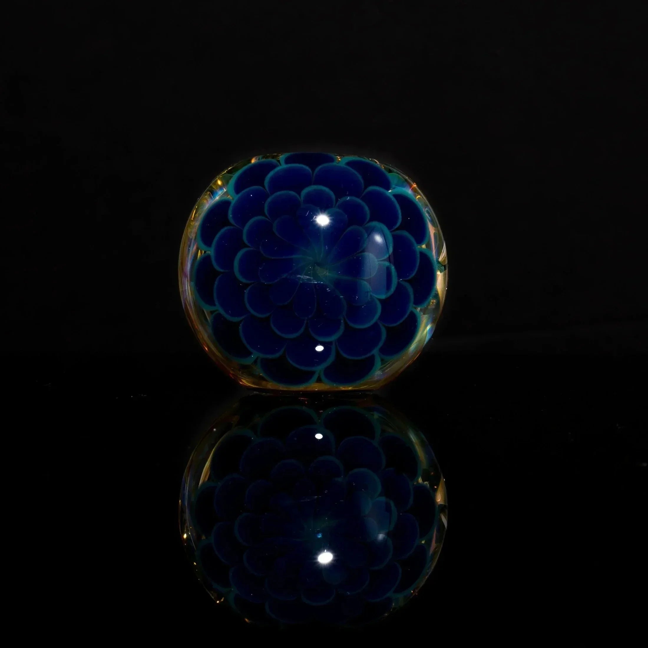 Handblown glass paperweight with blue floral design, reflective surface, dark background