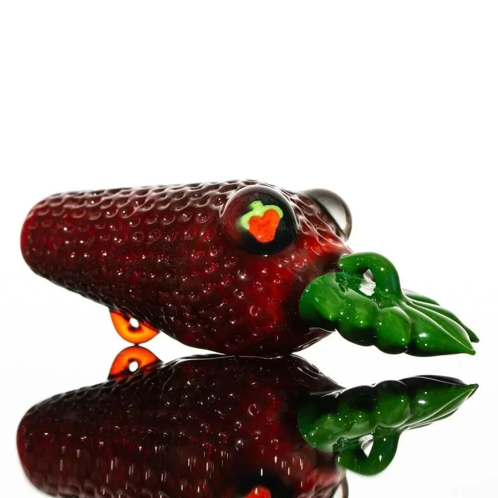 Hand-blown glass pipe shaped like a strawberry with green leaf detail on a reflective surface.