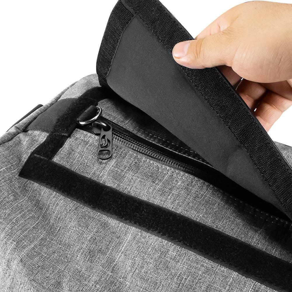 Close-up of a gray duffel bag with a hand opening the velcro flap, revealing a zippered pocket.