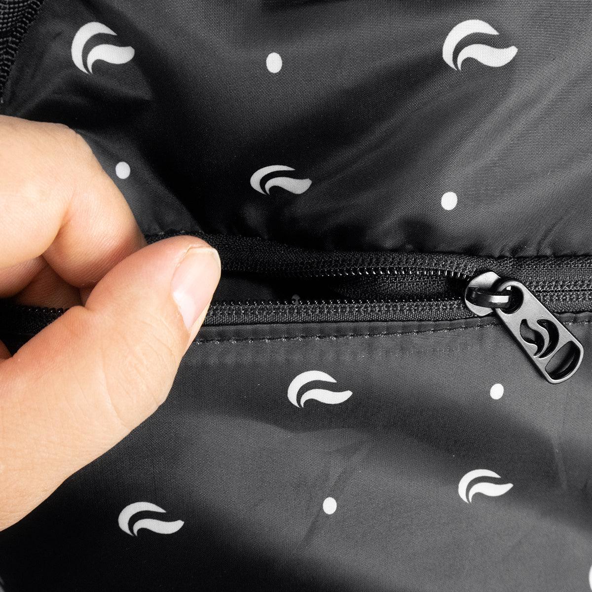 Close-up of a hand opening a mini backpack’s black interior pocket with zipper and printed pattern.