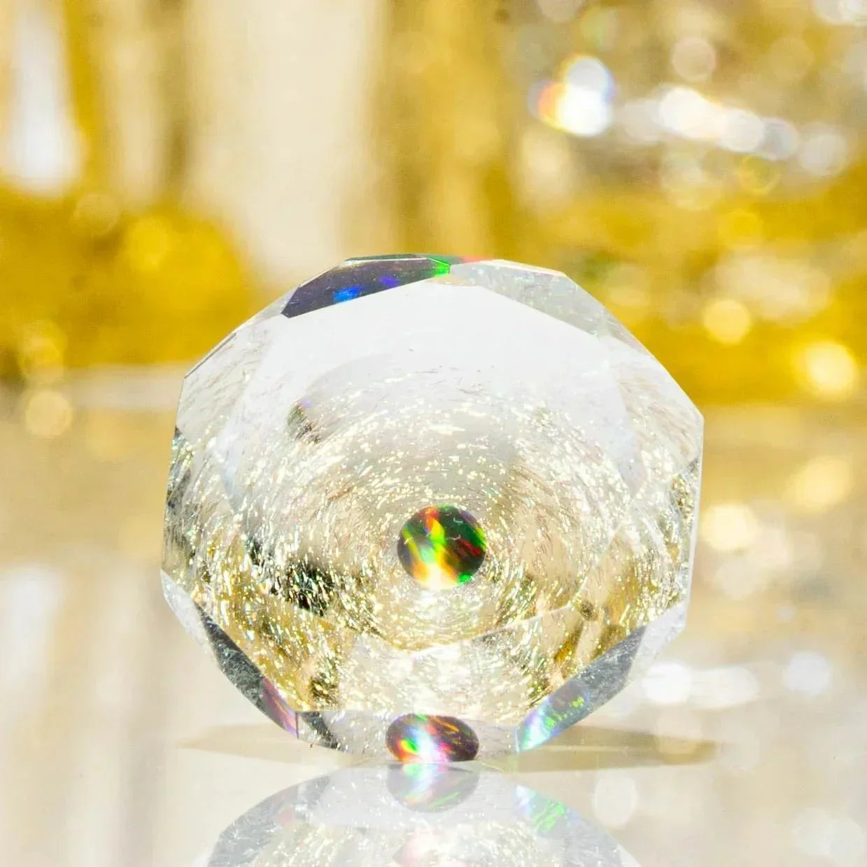 Faceted clear glass crystal sphere with rainbow reflections on a gold background
