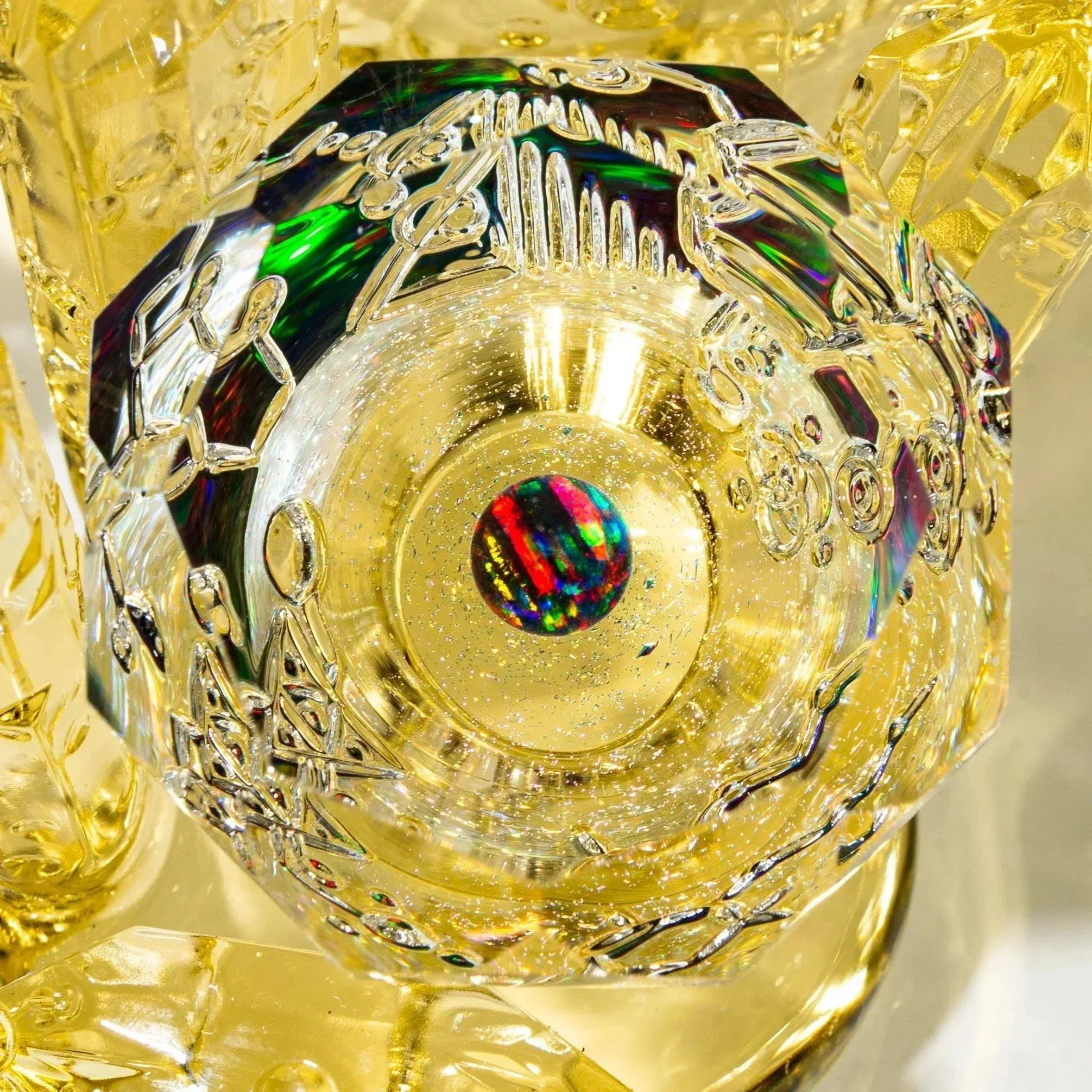 Close-up of intricate yellow glass art piece with etched designs and a multicolor opal accent