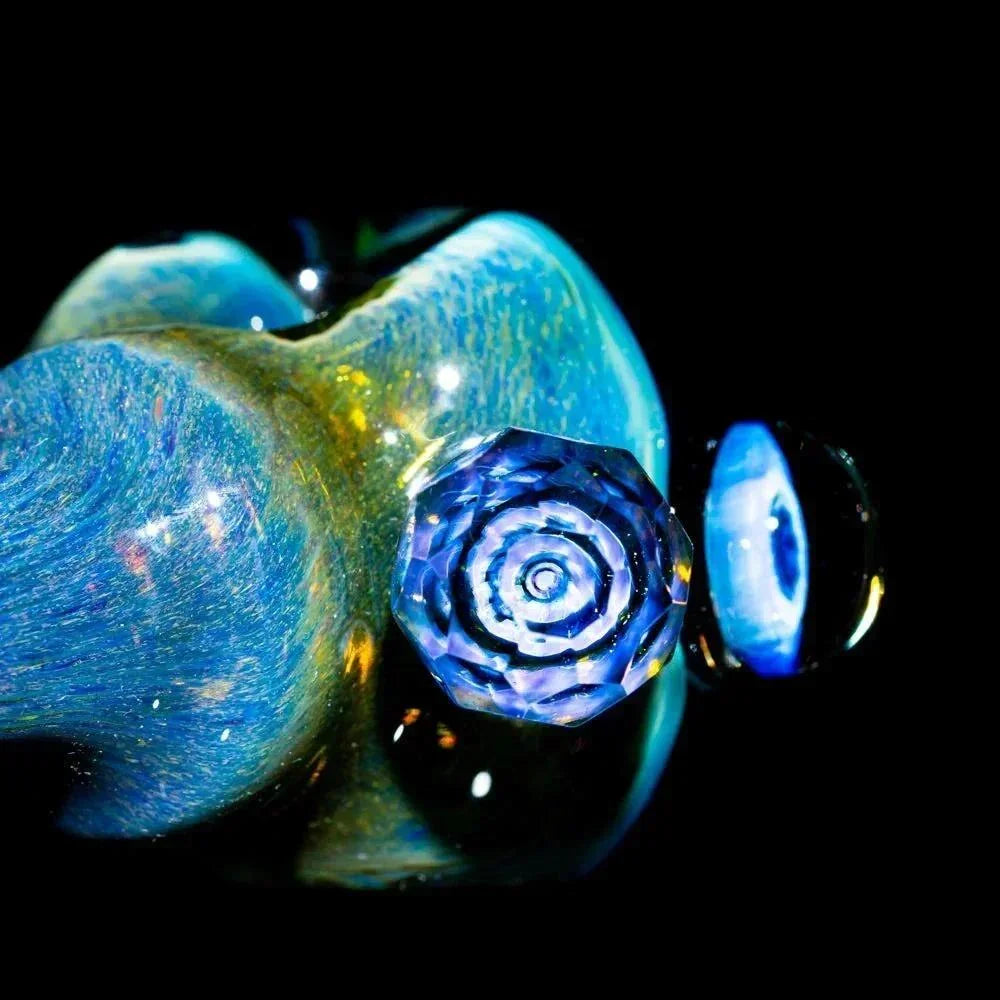 Close-up of a blue faceted glass spoon pipe with honeycomb pattern against a black background.
