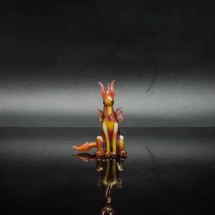 Hand-blown glass dragon figurine with vibrant orange and yellow hues, reflecting on a glossy surface.