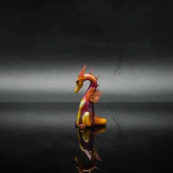 Colorful glass dragon figurine with vibrant orange, yellow, and purple hues on reflective surface
