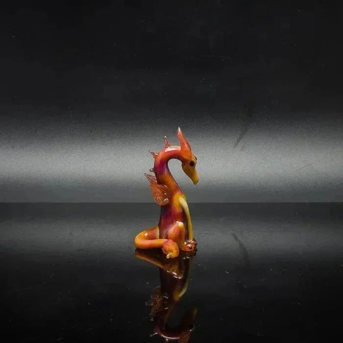 Vibrant glass dragon figurine with fiery orange and red hues, reflective surface, heady glass art