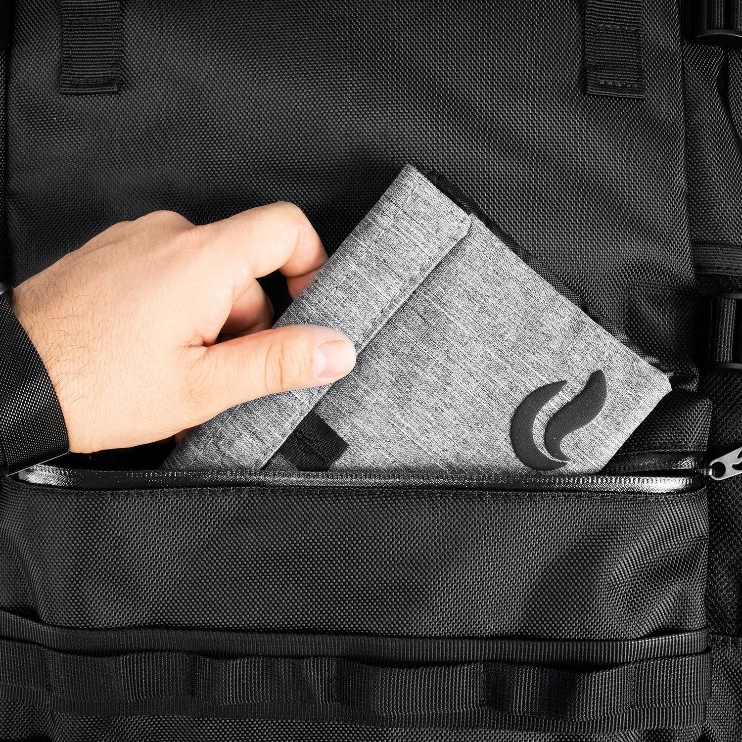 Hand placing gray fabric pouch with black logo into black backpack front pocket