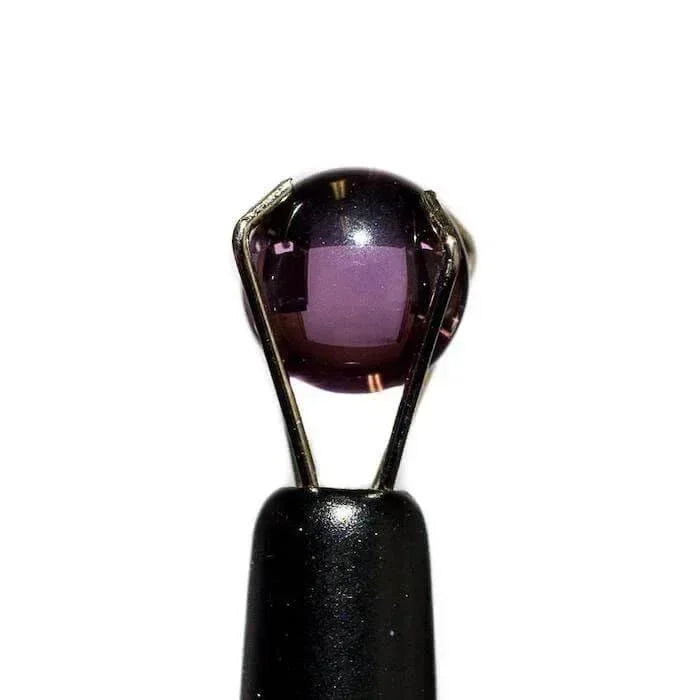 6mm round purple sapphire ruby pearl held by metal tweezers on white background