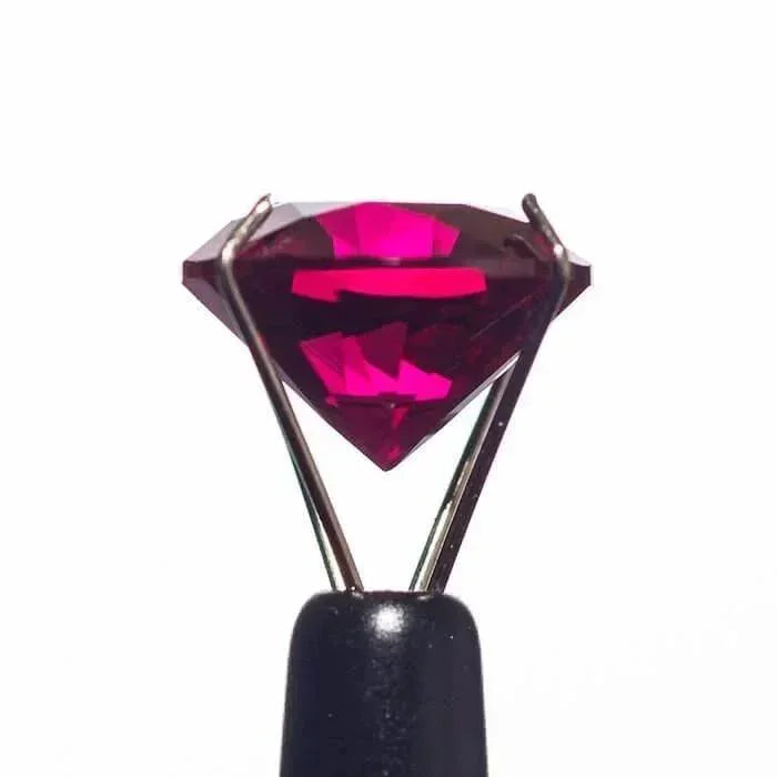 Faceted pink gemstone held by metal tweezers on black handle, ideal for glass pipe accessories
