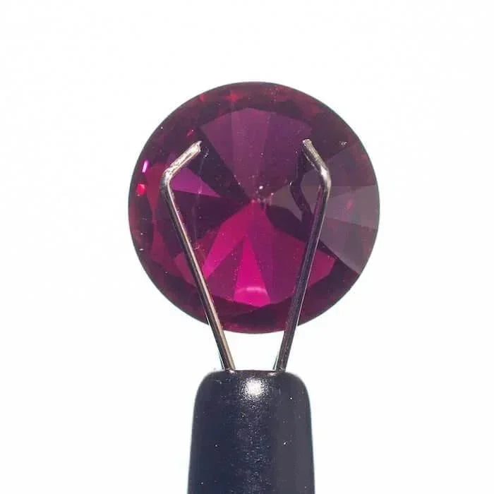 Faceted ruby gemstone held by tweezers, showcasing deep red sparkle for glass pipe accents