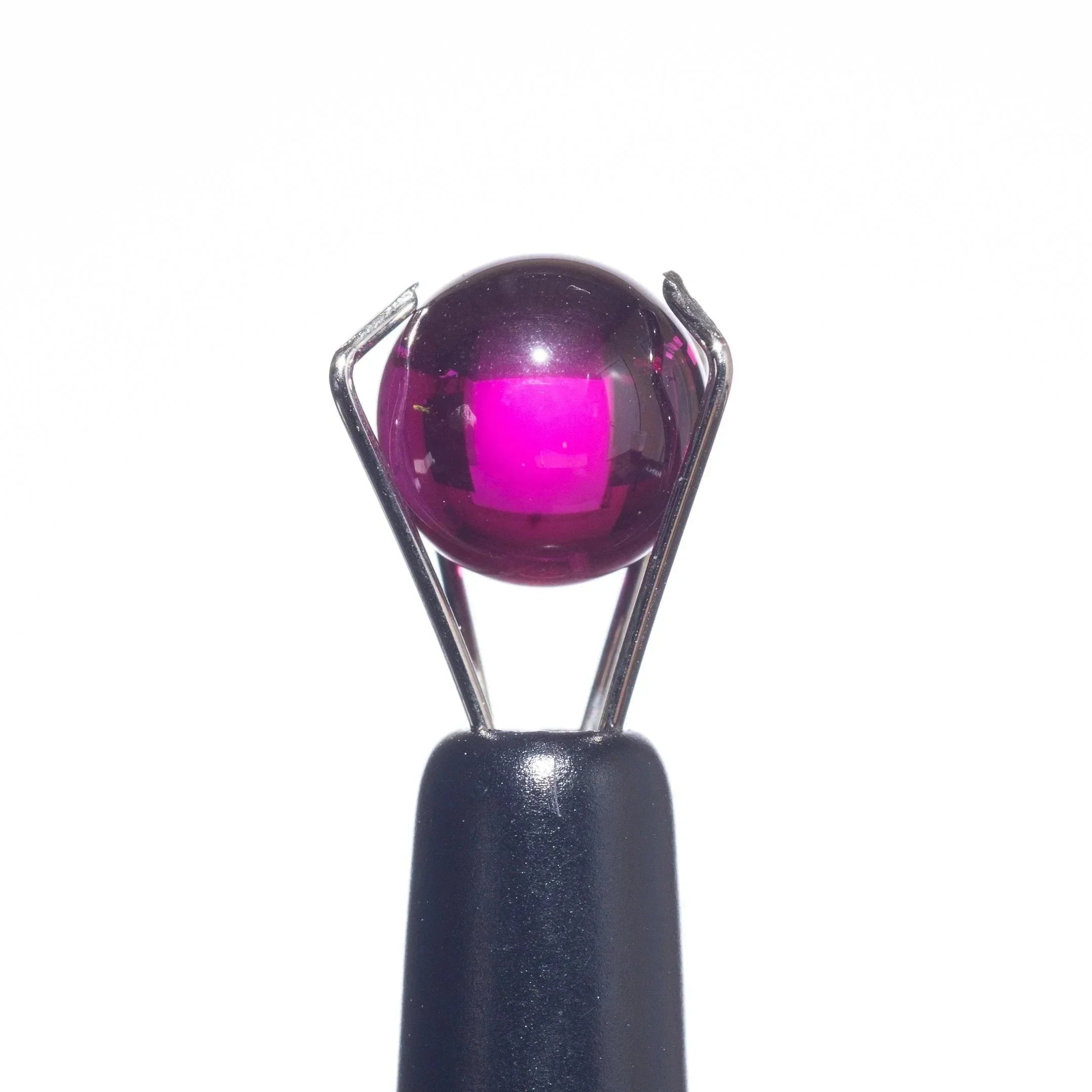 Vibrant pink glass marble held by metal tweezers, ideal for heady glass collections and vaporizer accessories.