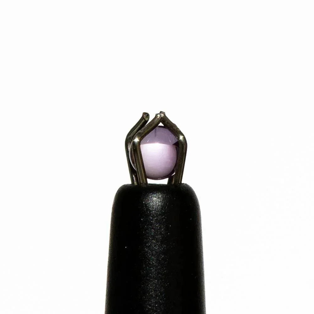Close-up of a small lavender glass terp pearl held by metal tweezers on a white background.