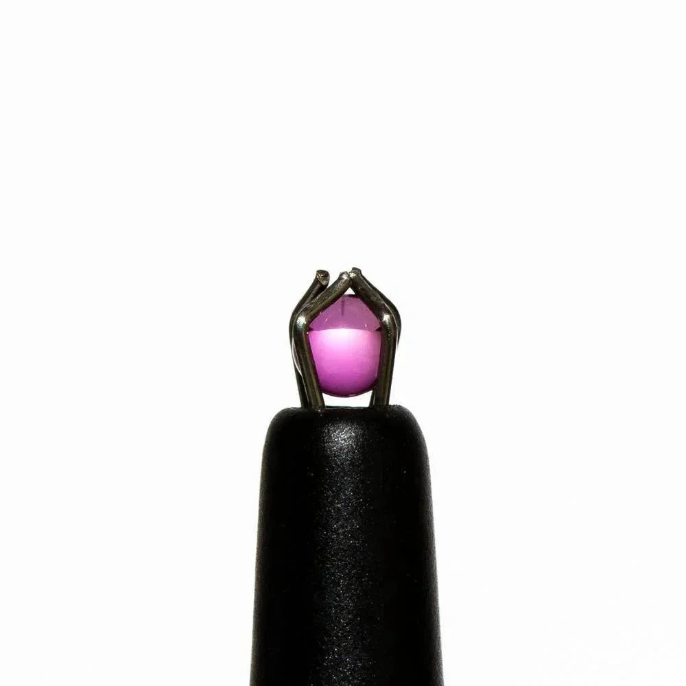 Close-up of a small round purple quartz terp pearl held by tweezers against a white background