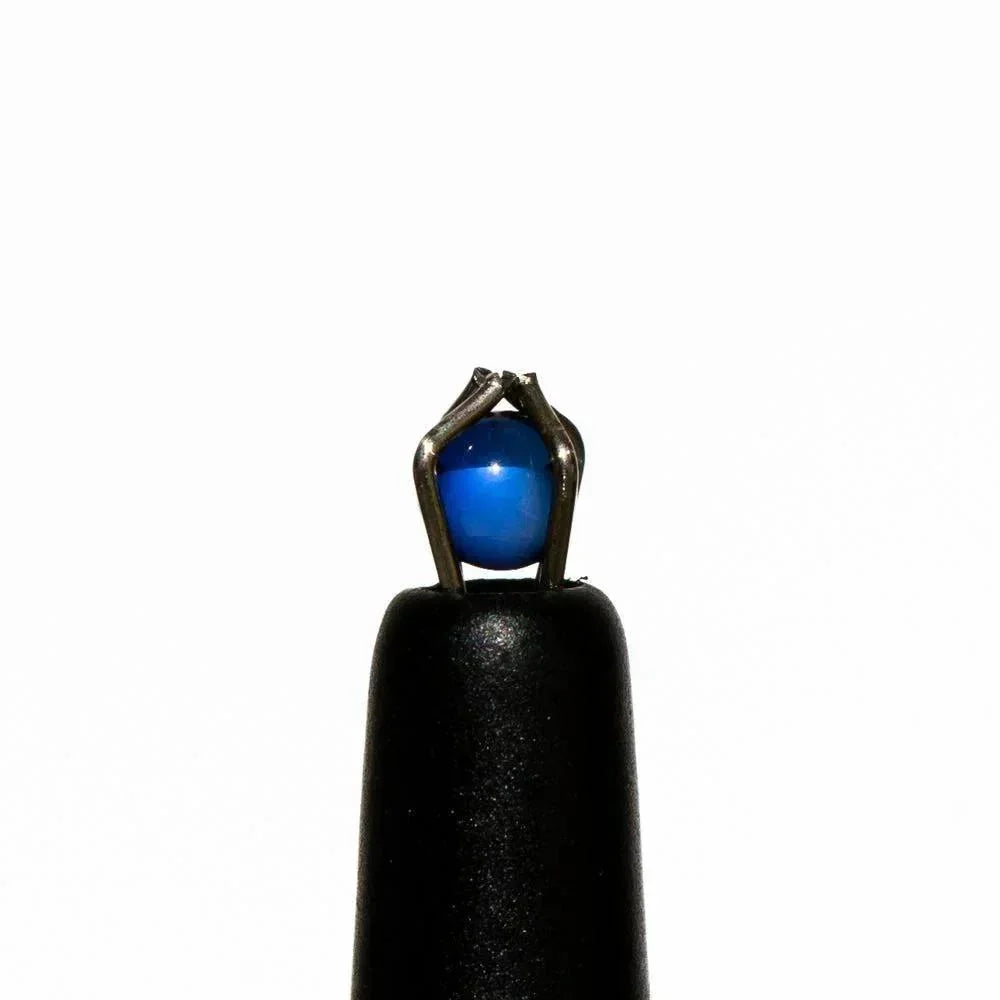 Close-up of a small blue sapphire terp pearl held by metal tweezers on a black stand