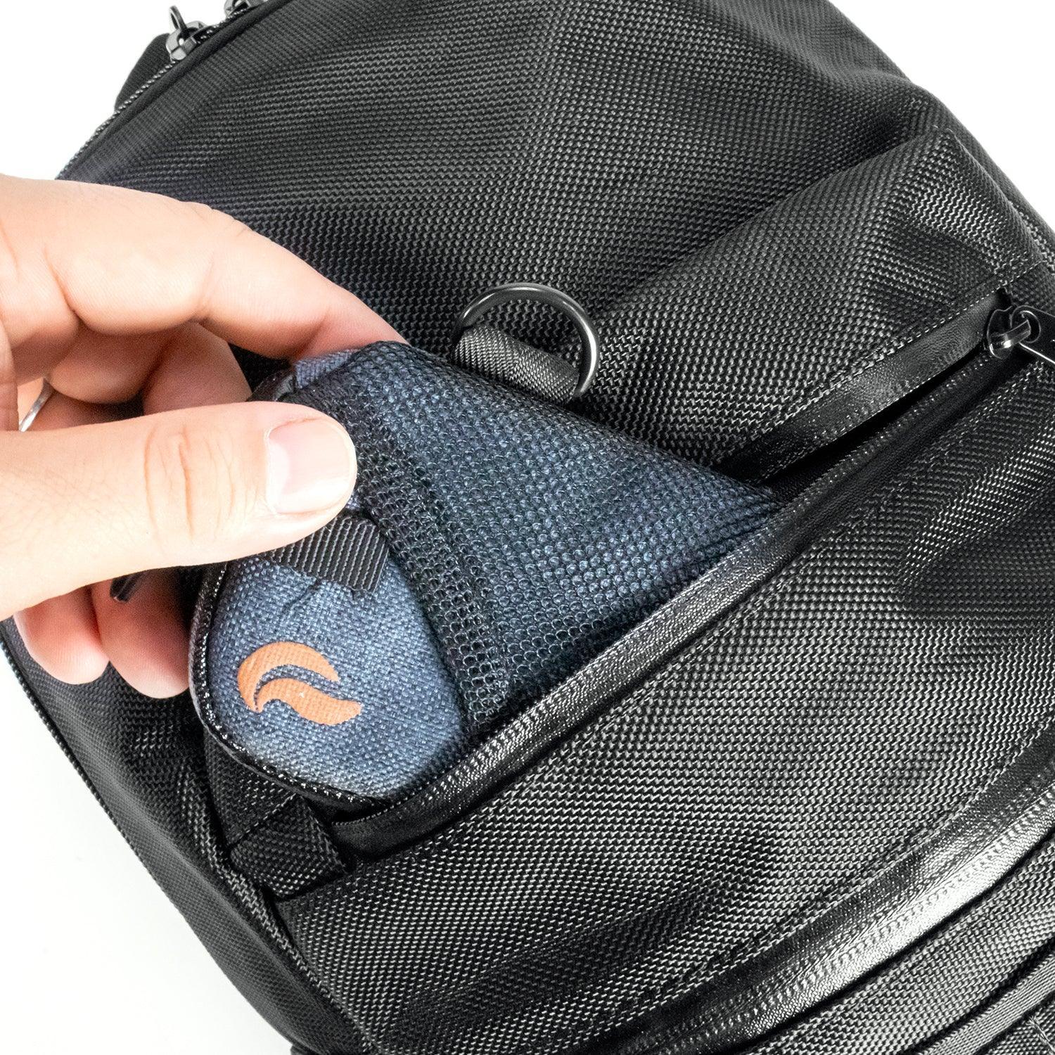 Hand placing small mesh pouch in front pocket of black textured backpack