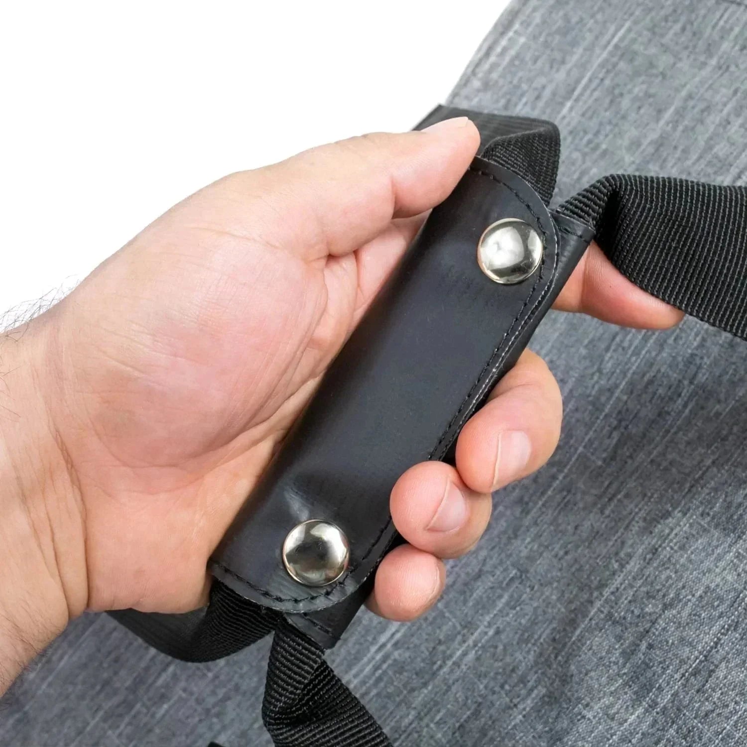 Hand holding a gray bag with padded black shoulder strap and metal rivets