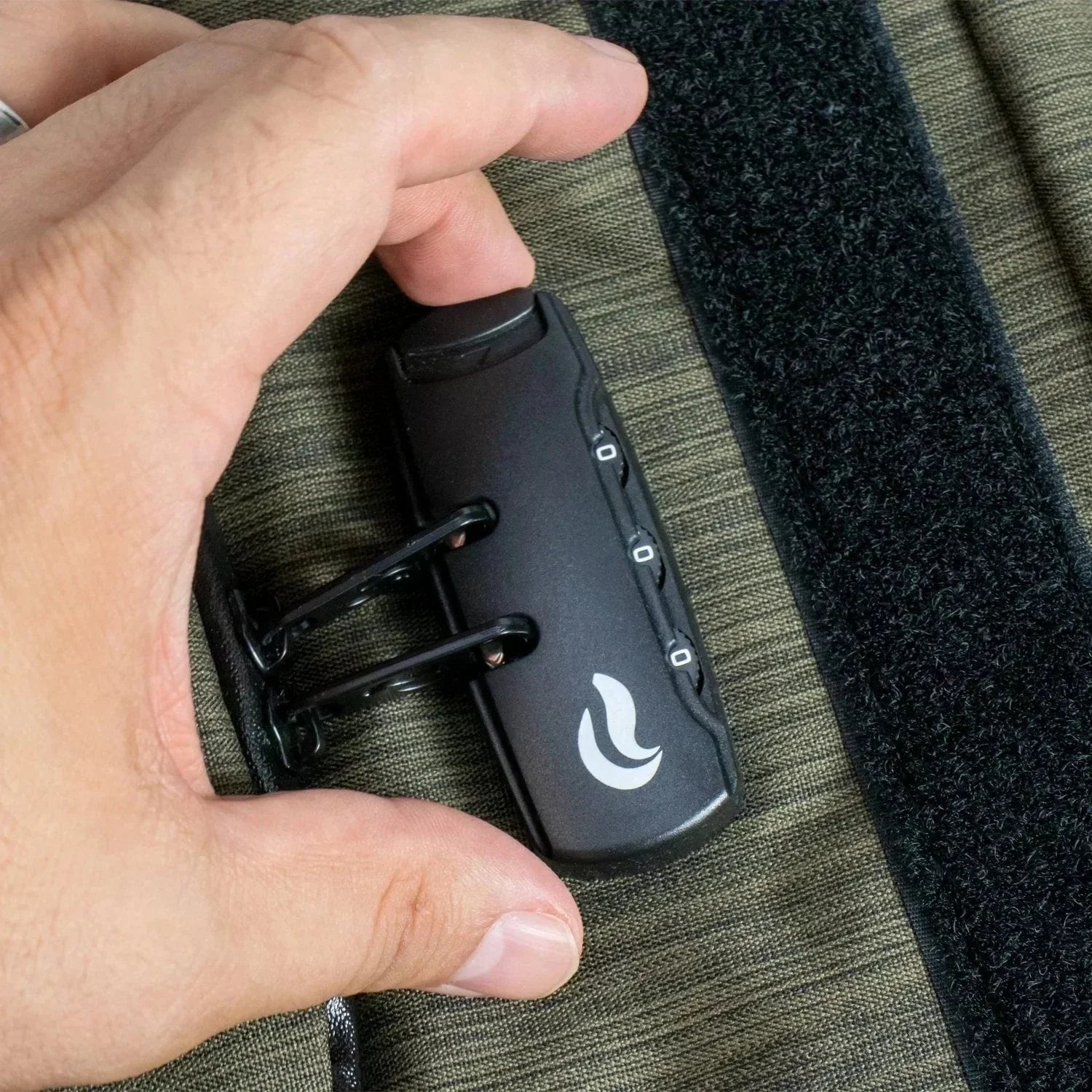 Hand holding a black combination lock on green fabric bag with velcro strip