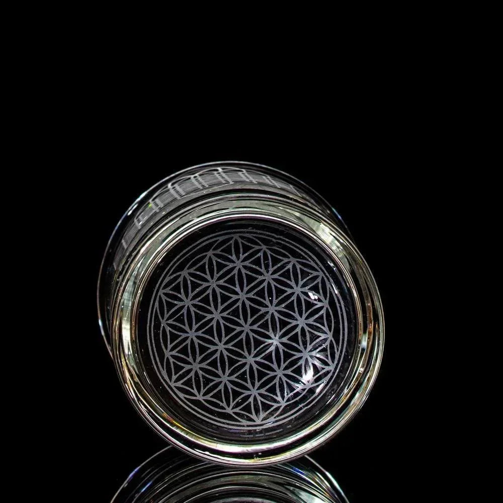 Clear glass cup with geometric etched flower pattern on the base, black background
