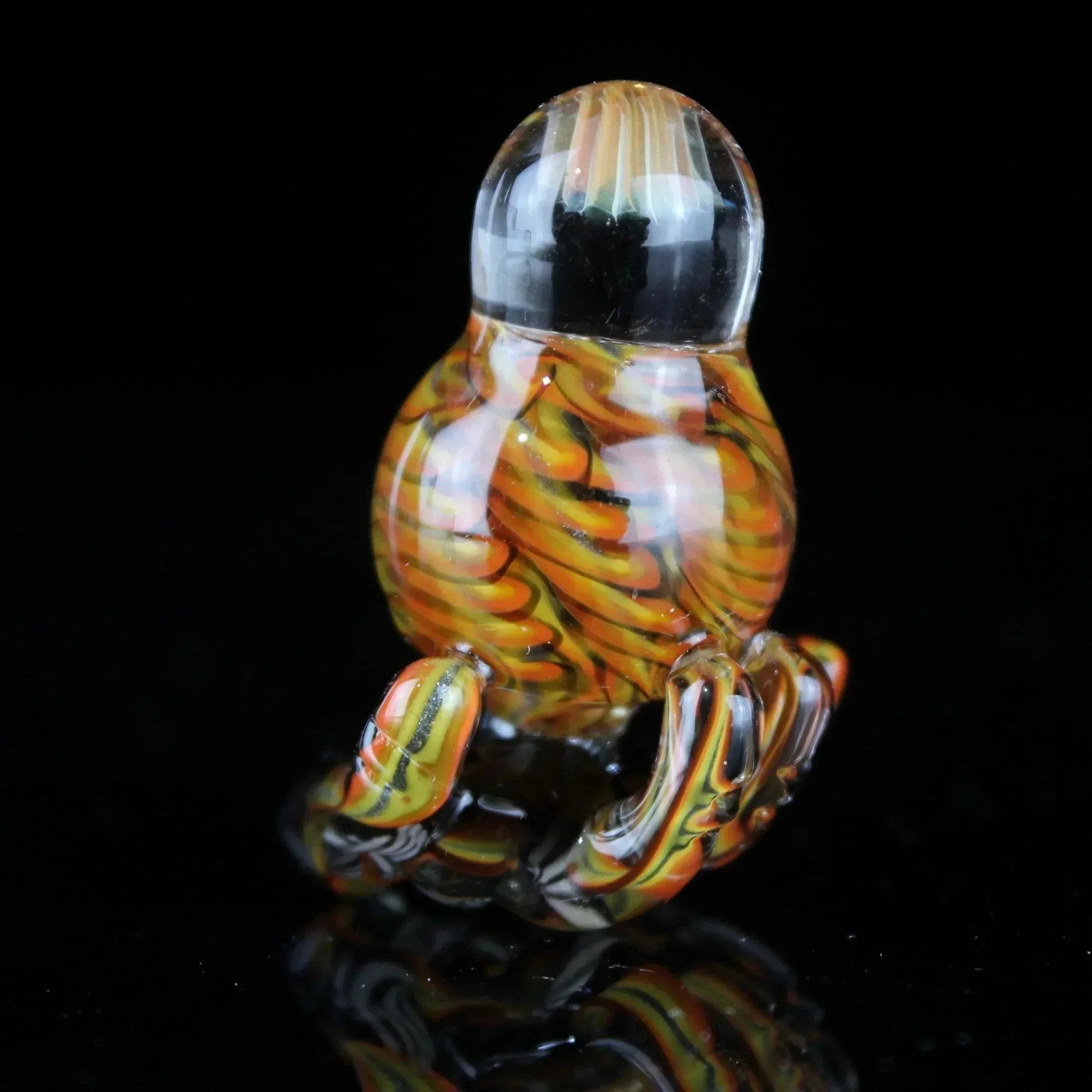 Hand-blown glass carb cap with orange, yellow, and black swirls on a glossy black background