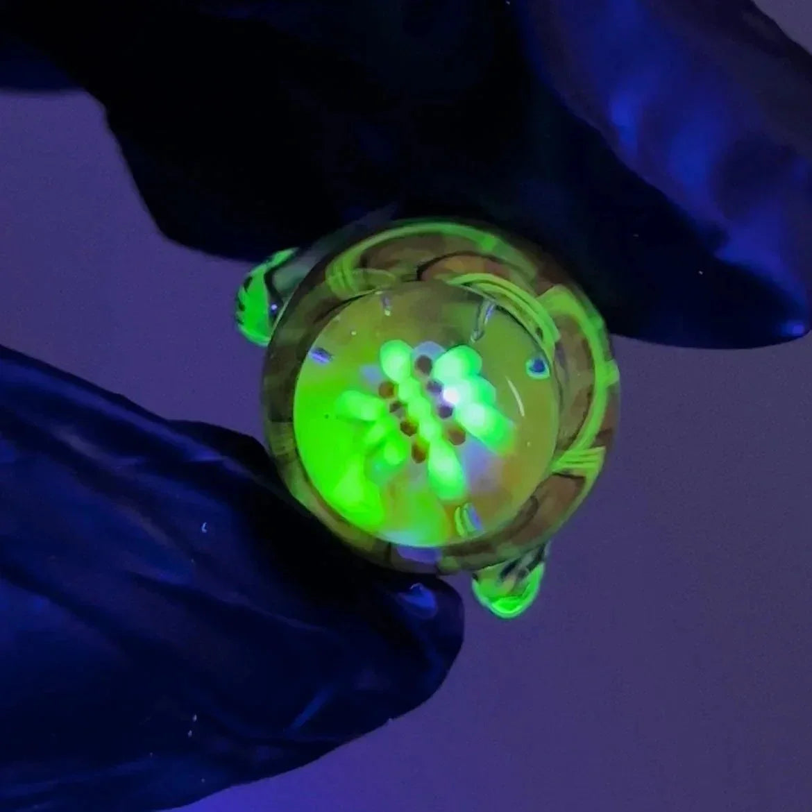UV reactive glass marble with green glowing design held by gloved hand under blacklight