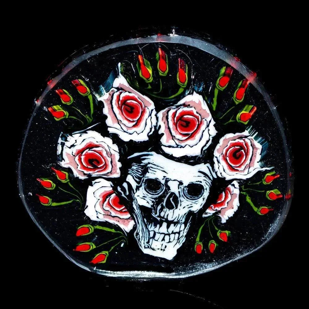 Glass coin featuring a skull surrounded by pink roses and green leaves on black background