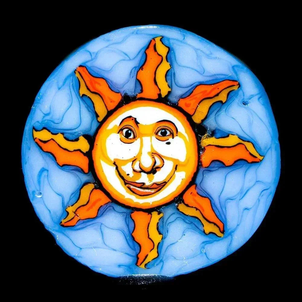 Handcrafted glass coin with a smiling sun face and orange rays on a blue background
