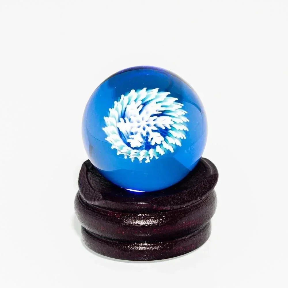 Blue glass marble with white snowflake design on a dark wooden stand, close-up
