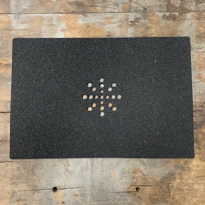 Black textured mat with starburst hole pattern on rustic wood surface