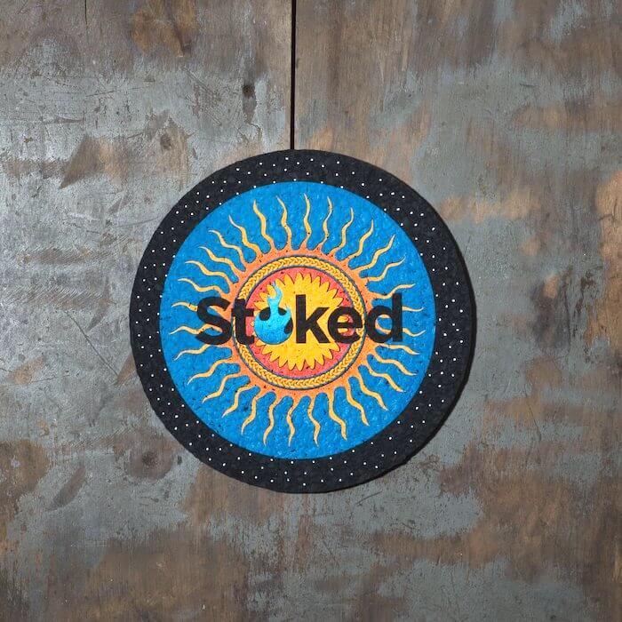 Stoked 8 inch mood mat on wood background. Blue and yellow sun logo centered