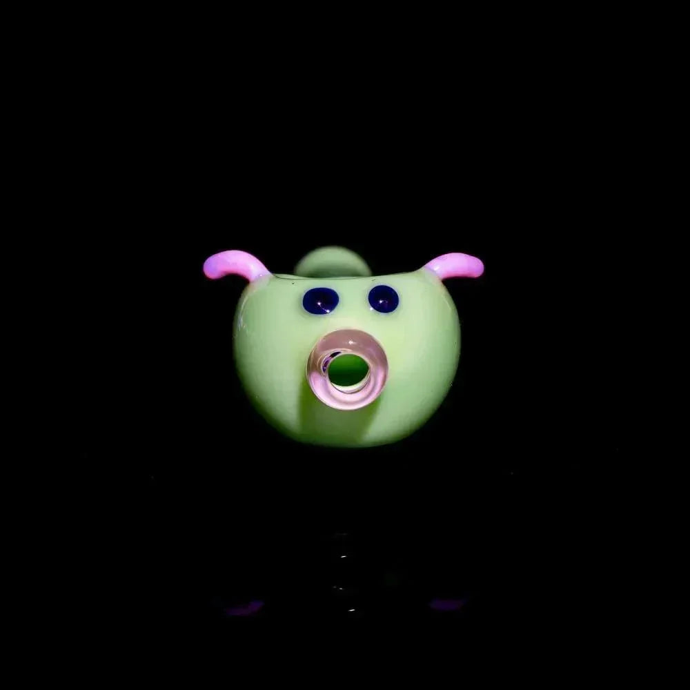 Milky green glass pig-shaped spoon with pink ears and blue eyes on black background