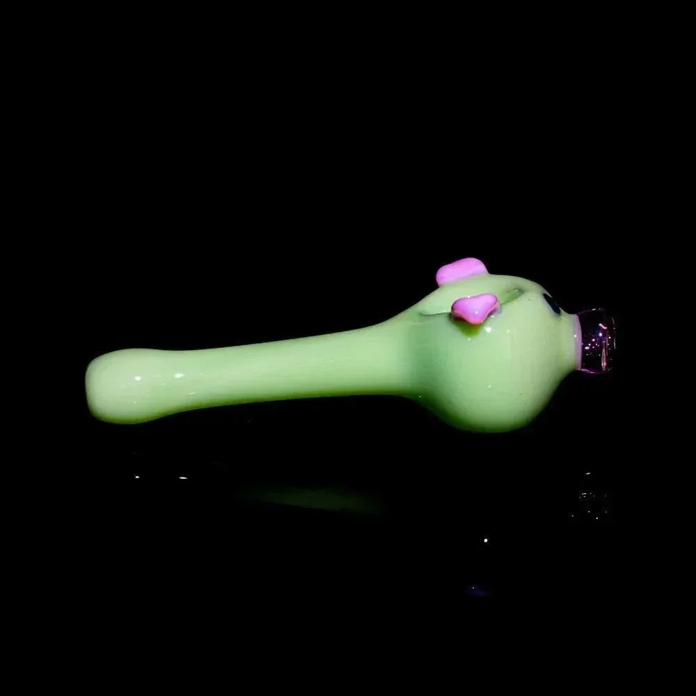 Milky green glass pig-shaped hand pipe with pink ears on a black background
