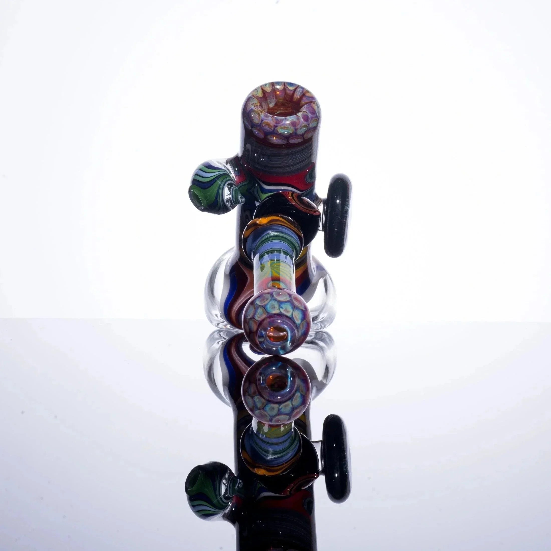 Colorful glass bubbler pipe with intricate patterns, displayed on reflective surface.