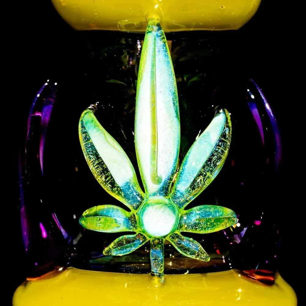 Close-up of a glass art piece featuring a glowing leaf design on vibrant yellow glass.