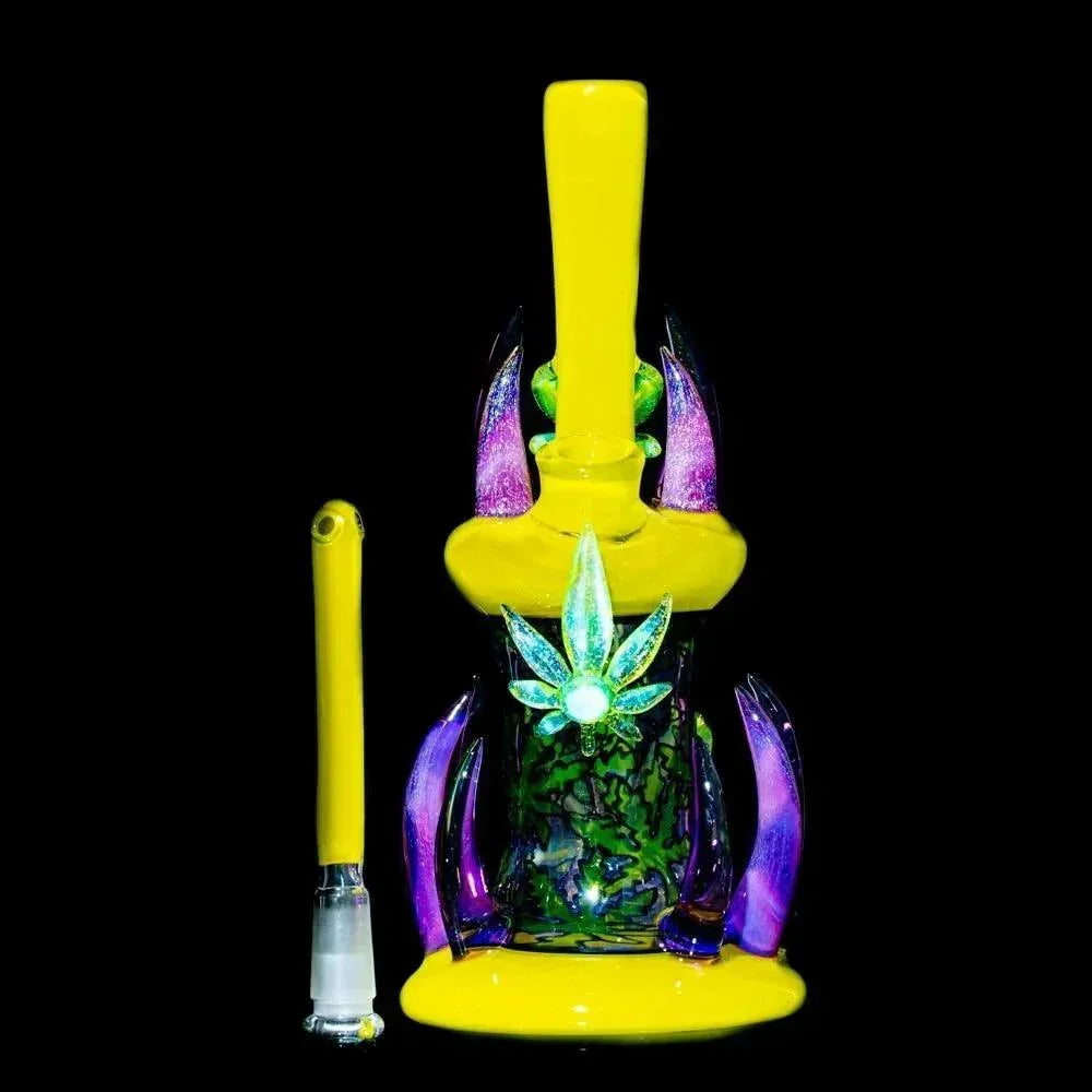 Heady glass rig with yellow accents, colorful leaf design, and matching dab tool on black background.