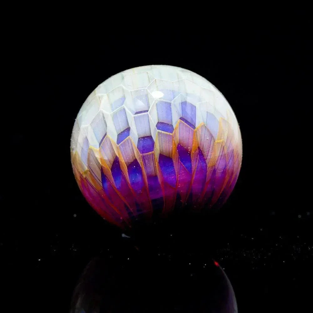 Intricately faceted glass marble with purple, gold, and white hues on black background