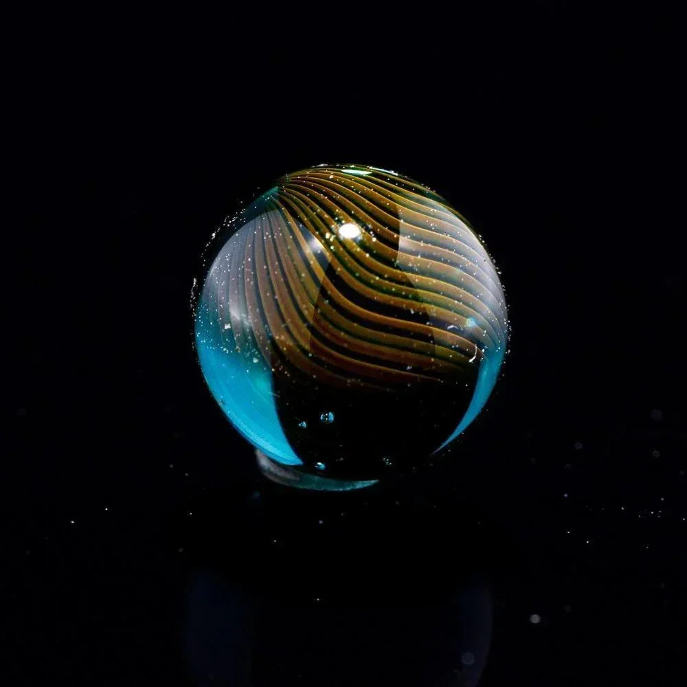 Handcrafted glass marble with swirling yellow and blue pattern on black background