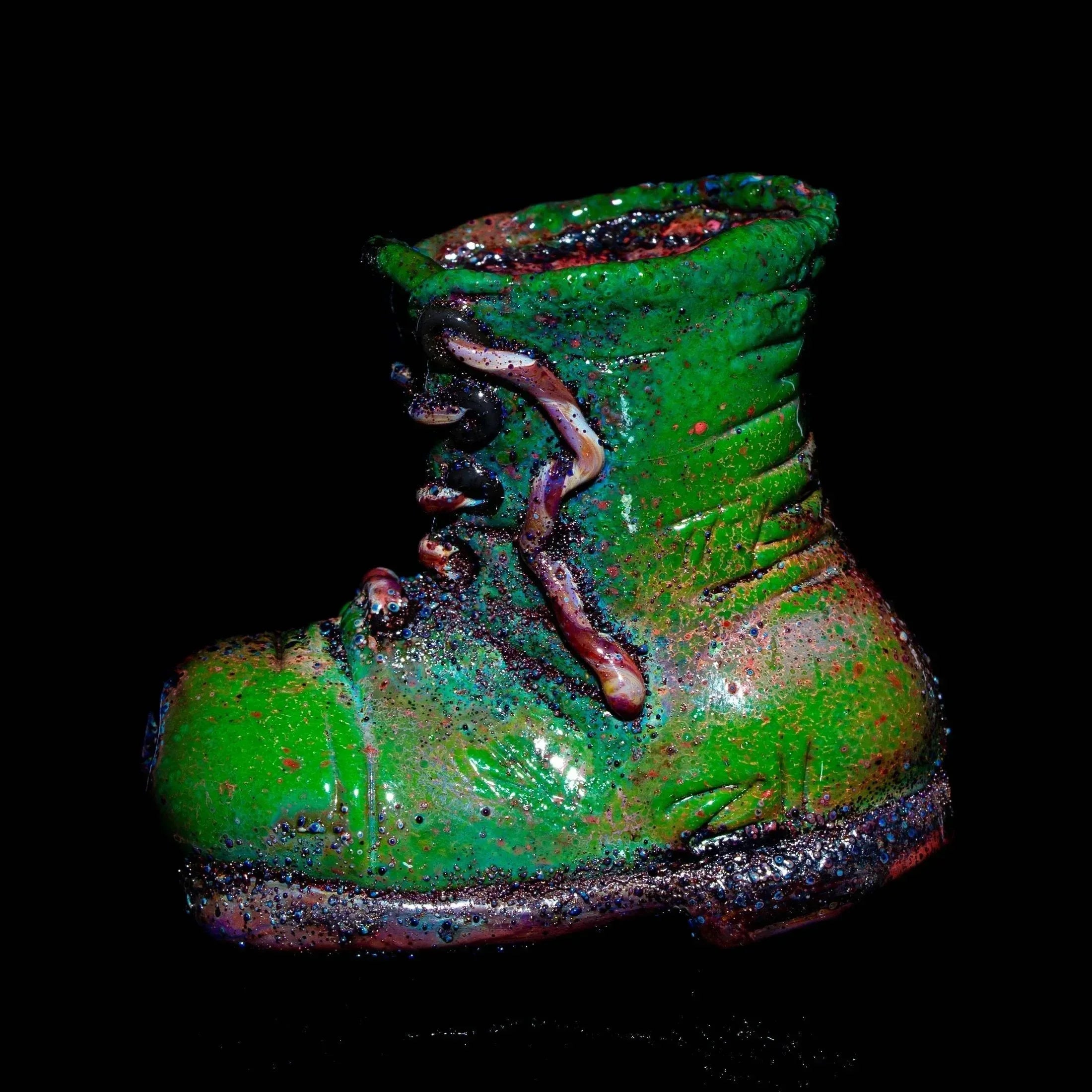 Colorful glass boot-shaped smoking pipe with speckled design on black background