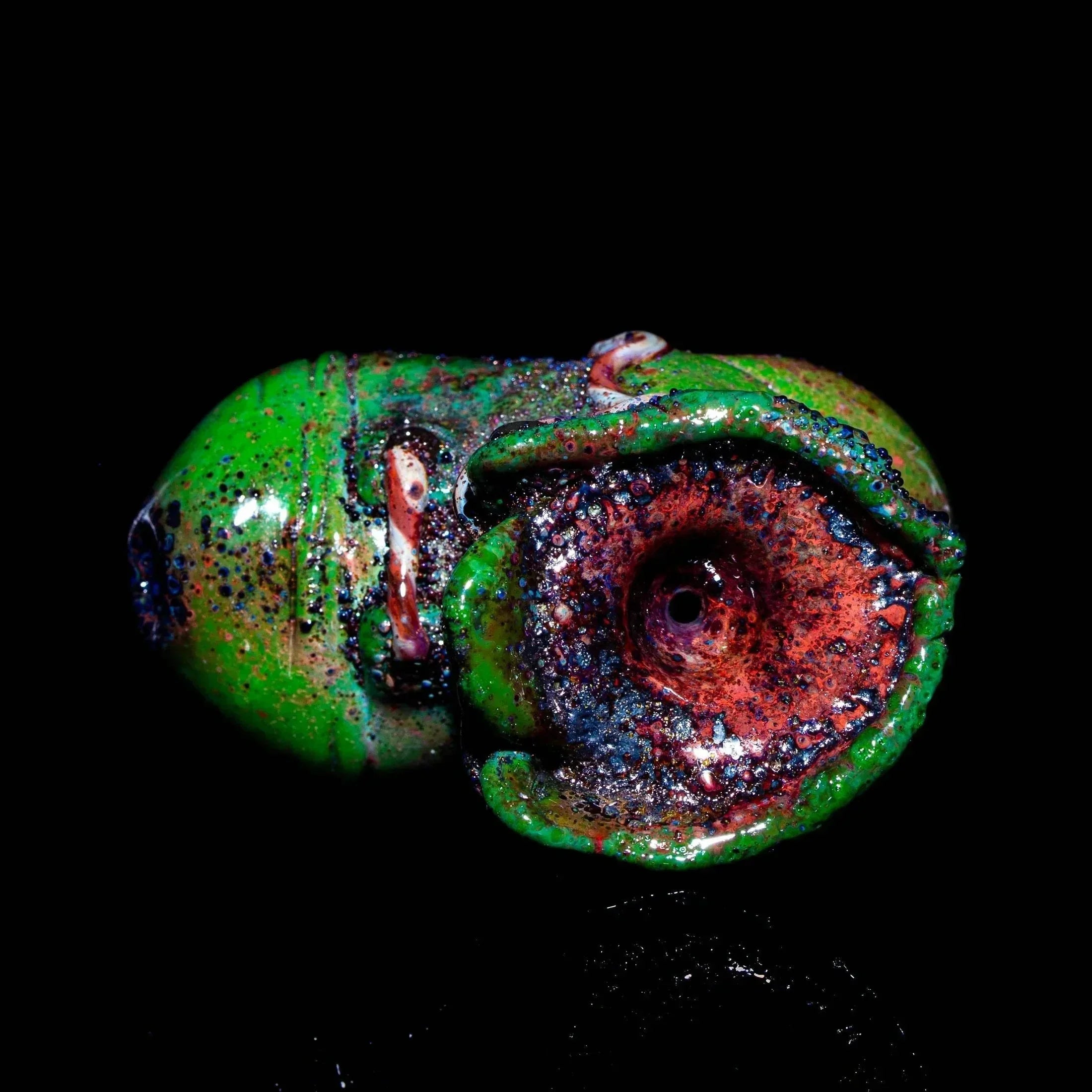 Handcrafted green glass dry pipe with textured red and blue bowl on black background
