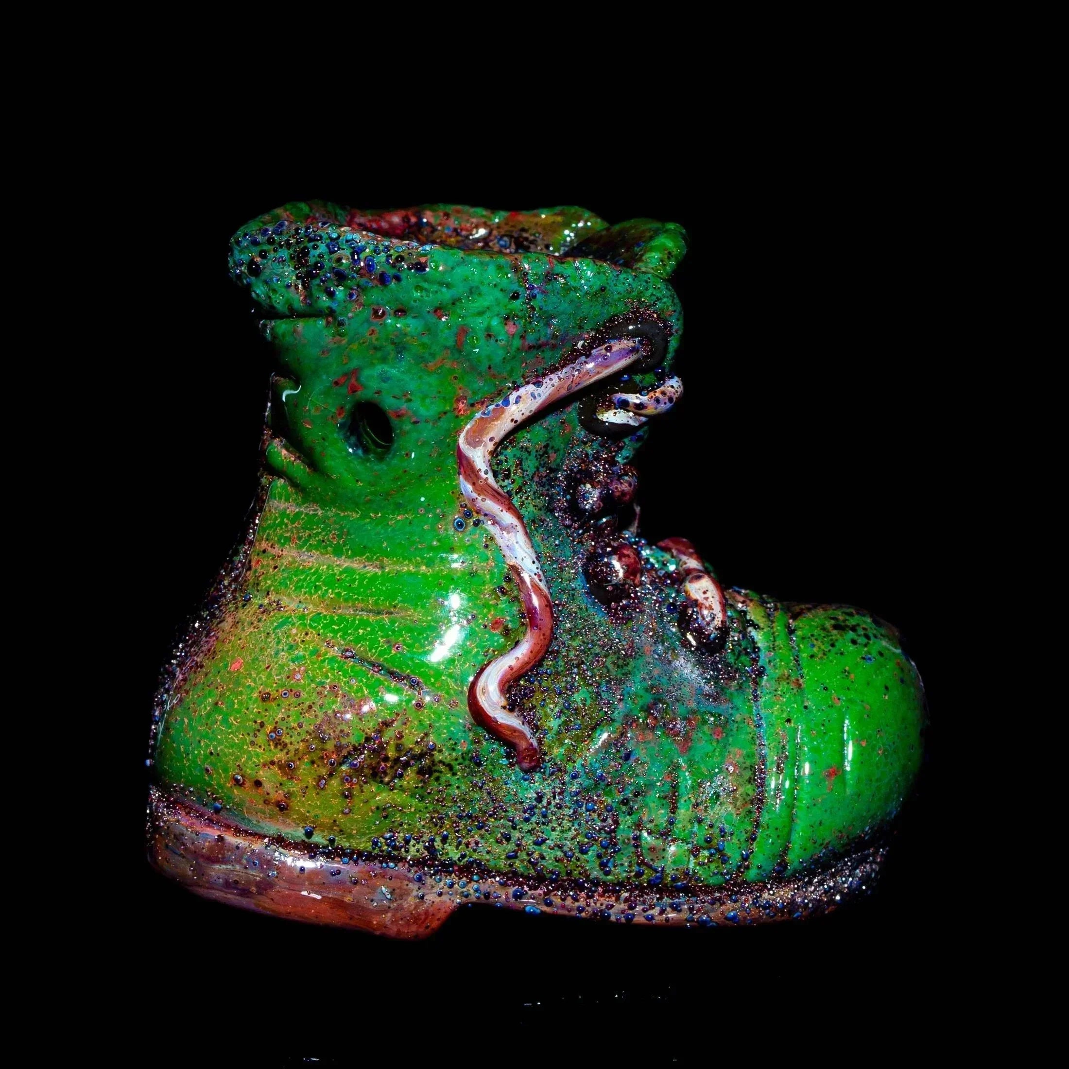 Colorful glass dry pipe shaped like a green boot with speckled details on black background.