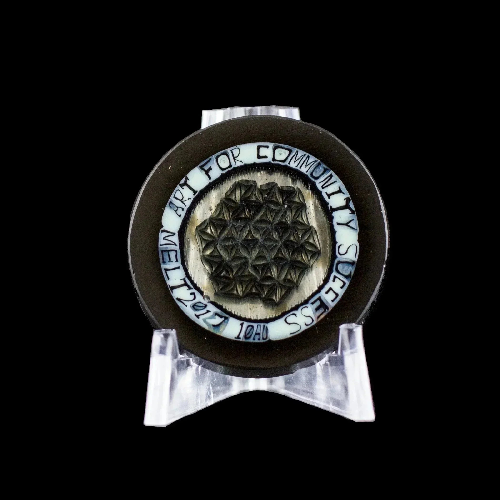 Artistic glass piece with geometric design and 'Art for Community Success' text, displayed on stand