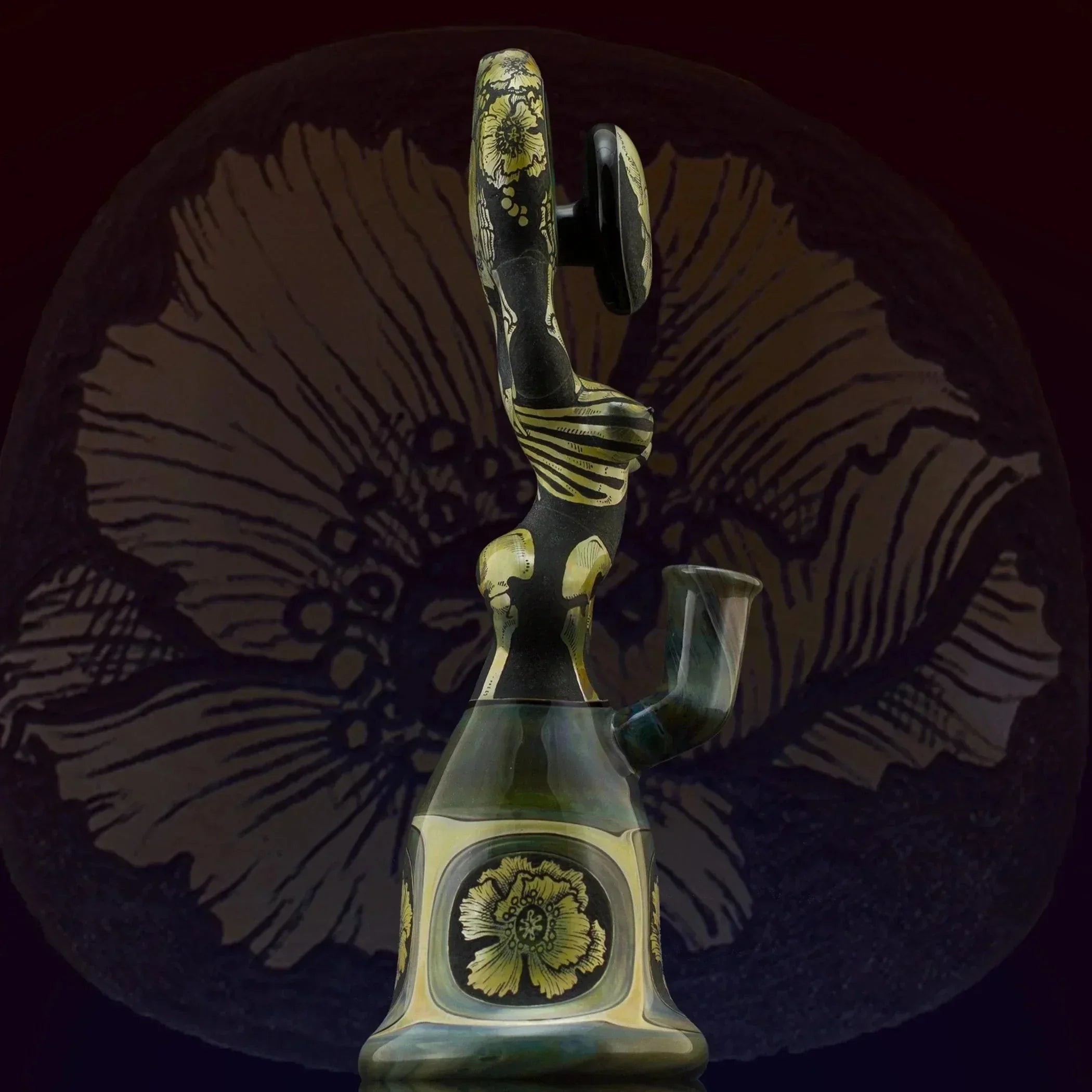 Artistic glass bong with gold floral designs and intricate detailing, set against a dark floral backdrop.