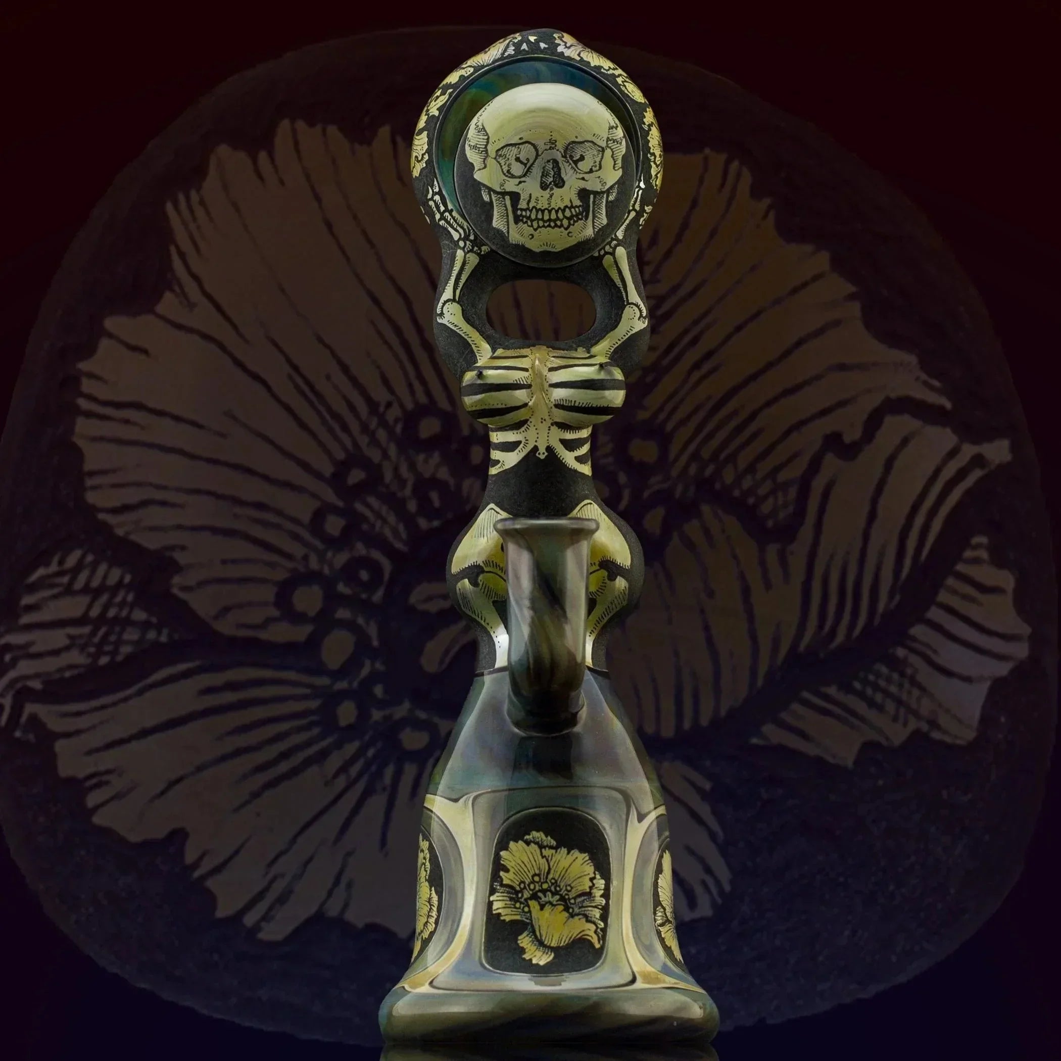 Artistic glass pipe with skull and skeleton design, featuring gold accents and floral motifs on dark background