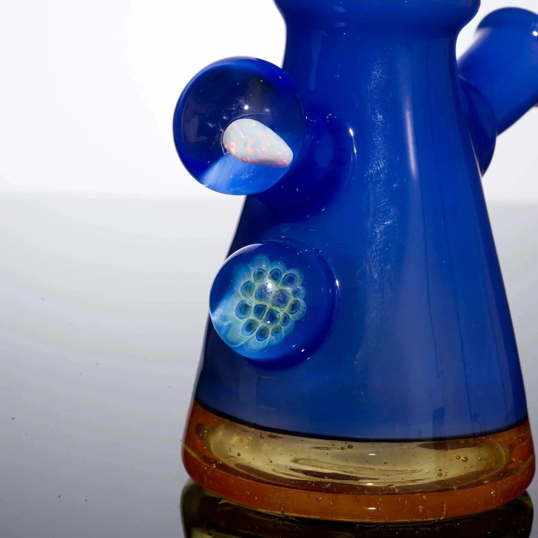 Vibrant blue glass bong with intricate floral inclusions and amber base, showcasing heady glass artistry.